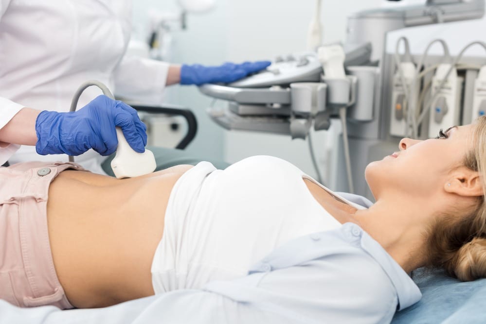 A woman is having an ultrasound scan in a private clinic in London. The sonographer is resting an ultrasound probe on her abdomen