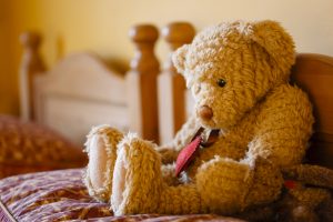A sad teddy bear sitting on an empty bed